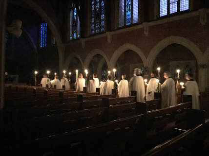 Choir carrying lit candles processing up the aisle in a dark church